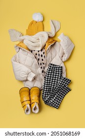 Kids warm puffer jacket with hat and boots on yellow  background. Stylish childrens outerwear. Winter fashion outfit 