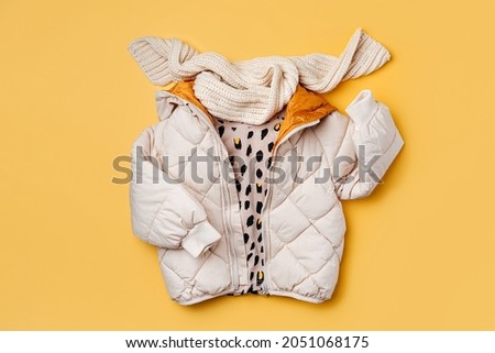 Kids warm puffer jacket with scarf on yellow  background. Stylish childrens outerwear. Winter fashion outfit 