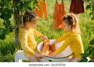 Kids Wash Clothes In A Basin On A Bench In The Garden. Girls Have Fun Helping With Housework. Washing Powder For Washing Baby Clothes. 