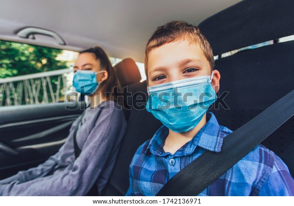 Kids\
wearing anti virus masks and using digital tablets in the car. Kids\
are travelling in car during coronavirus\
outbreak