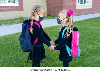 Kids Wearing Cotton Mask And Backpacks As Safety From Coronavirus Back To School. Two Sister Holds Hands Together Support Against Virus . New Normal For School Year. Two Student Girls Near School.