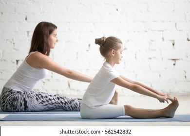 Kids yoga female teacher training a girl child, two people practicing yoga, sitting in paschimottanasana exercise, seated forward bend pose, working out wearing sportswear, indoor, white studio  - Powered by Shutterstock