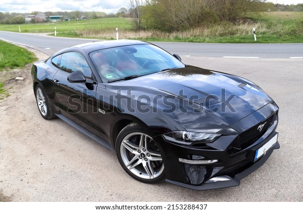 Kiel, Germany - 30.April 2022: High angle front view\
on a black Ford Mustang model 2018 sports car parked on a sandy\
road