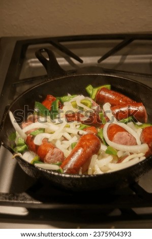 Kielbasi, onions and peppers, cooking in a castiron frying pan on a gas stove