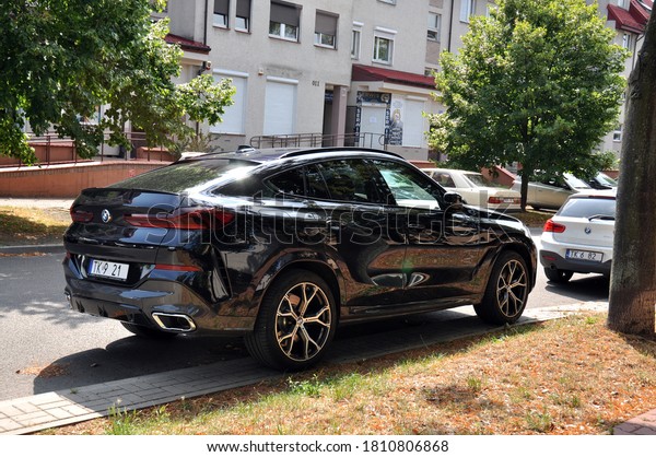 Kielce, Świętokrzyskie /\
Poland 2020-08-19 Parked black car bmw on the roadside view of\
residential buildings and shops in the distance (part of\
registration erased)