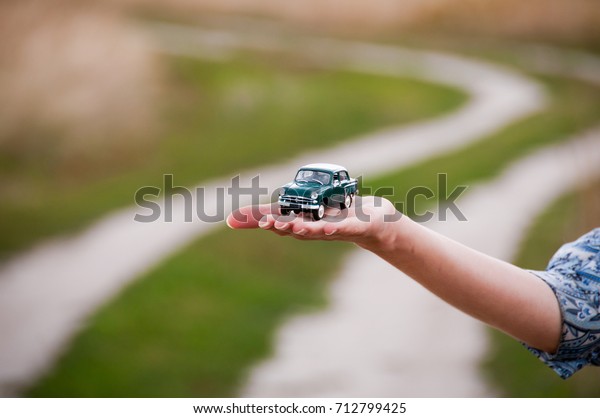 KIEV,\
UKRAINE - JULY 10, 2017: Toy retro car in the woman\'s hand on a\
road background. Concept of safe driving. Car insurance. Woman\'s\
hand holding classic mini model. Space for text.\
