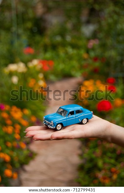 KIEV,\
UKRAINE - JULY 10, 2017: Toy retro car in the woman\'s hand on a\
road background. Concept of safe driving. Car insurance. Woman\'s\
hand holding classic mini model. Space for text.\
