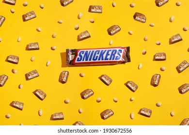 Kiev, Ukraine - March 6, 2021: Pieces of Snickers chocolate bar on a background of peanuts. Modern composition on yellow background 
