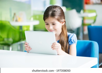 KIEV, UKRAINE - MAY 21, 2014: Little smiling  girl sitting at the desk and looking on a brand new Apple iPad Air. Apple iPad Air developed by Apple inc. and was released on November 1, 2013.
