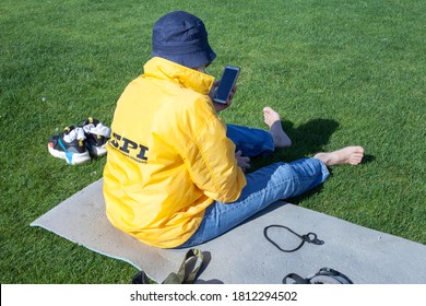 KIEV, UKRAINE - SEPTEMBER 10, 2020: A Woman In A Bright Yellow Jacket And A Panama Hat Is Sitting On A Green Golf Course After A Game On A Sunny Day. Back View