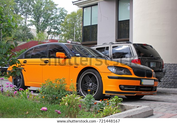 Kiev, Ukraine - September 2, 2017: BMW 7 Series\
Alpina in an orange matte film against the background of other cars\
and a house