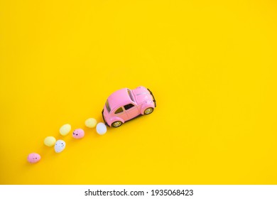 Kiev, Ukraine-March 13, 2021: Retro toy pink car with Easter egg on the roof. Easter card with space for text on a yellow background. Easter grocery delivery
