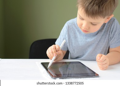Kiev/Ukraine - 02.26.2019 White caucasian smiling toddler boy drawing on the screen of iPad Pro with white pencil. Portrait of happiness cute little boy with tablet. Boy playing game on tablet