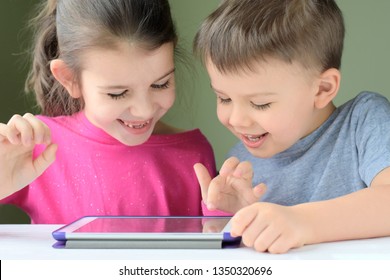 Kiev/Ukraine - 02.26.2019 White caucasian toddler boy and beautiful girl playing together on tablet games. Portrait of smiling little brother and sister. Children play game and drawing on iPad tablet