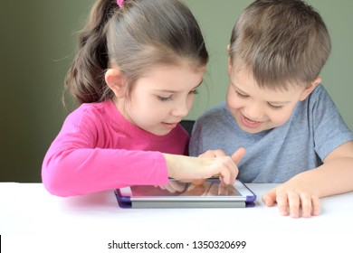 Kiev/Ukraine - 02.26.2019 White caucasian toddler boy and beautiful girl playing together on tablet games. Portrait of smiling little brother and sister. Children play game and drawing on iPad tablet