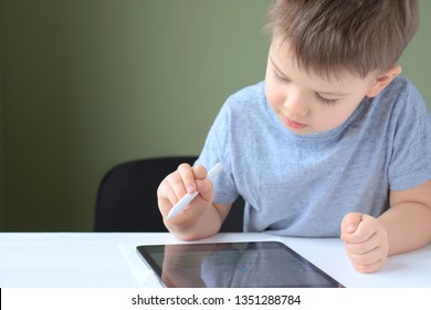 Kiev/Ukraine - 02.26.2019 White cute smiling toddler boy drawing on the screen of iPad Pro with apple pencil. Boy playing game on iPad. Portrait of happiness caucasian little boy with IPad tablet.
