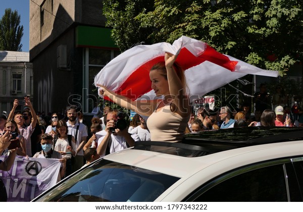 Kiev/Ukraine - 08.16.2020:young beautiful\
woman political activist stand in car with red white national\
Belarusian flag in hands above the head during street action for\
free Belarus against\
Lukashenko