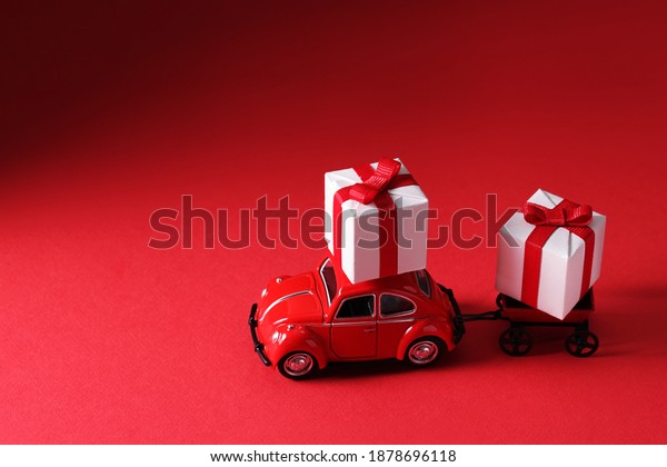 Kiev,Ukraine, December,12,2020: Red car delivering gifts\
box on red background. Concept Logistic. Surprise for loved one.\
Valentine\'s day, weddings, birthday, New Year, Christmas, dad or\
mom 