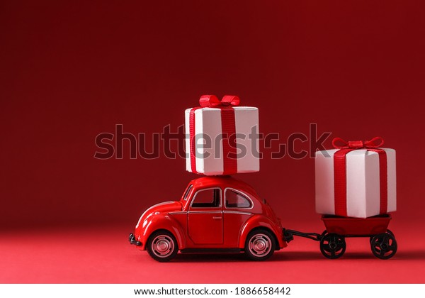 Kiev,Ukraine,\
January,03,2021: Red car delivering gifts box on red background.\
Surprise for loved one. Delivery Concept. Buying online gifts.\
Valentines day, weddings, birthday, mom\
day