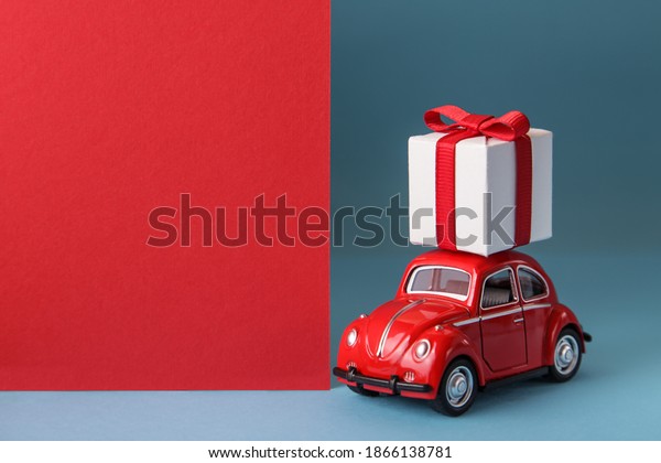 Kiev,Ukraine, October,30,2020: Red car\
delivering gift box on blue background. Christmas holiday\
celebration concept. Valentine\'s day concept. Copy\
space