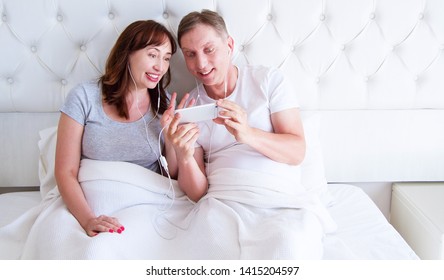 Kiev,Ukraine-09.10.2018: Apple Ear Pods.  Happy Middle Age Couple In Bed Using Cellphone  - Watch Video Or Talking On Video Chat, Happy People, Middle-aged Couple Bedroom