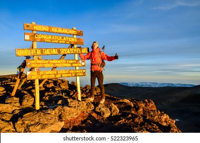 Kilimanjaro, Tanzania - March 11, 2015: A hiker standing on Uhuru Peak, the summit of Kibo and highest mountain in Africa, Mount Kilimanjaro at 5895m amsl. Summit sign and glacier in the background. 