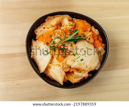 Kimchee in black bowl on wooden table. Spicy kim chi, hot fermented napa cabbage, traditional jimchi, korean winter food gimchi, kimchee on white background top view