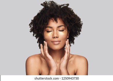 Kin Care. Attractive Young African Woman Applying Medical Eye Patch And Smiling While Standing Against Grey Background