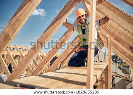 Kind bearded man keeping smile on his face while working on construction site