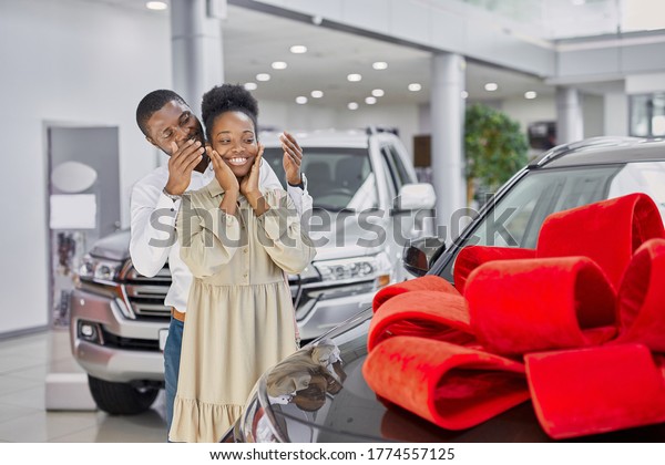 kind black man\
gave a car to his wife, the car is wrapped in a red bow, man closed\
woman\'s eyes, prepared\
surprise