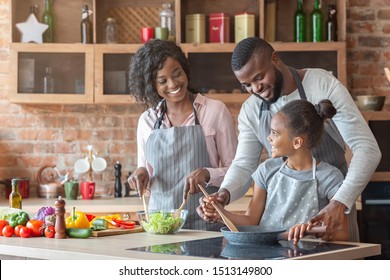 Kind black parents teaching their adorable daughter how to cook healthy food, kitchen interior, copy space