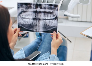 Kind brunette female holding X-ray picture, being at stomatology while doing tooth checkup