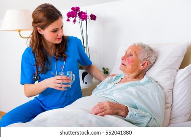 Kind geriatric doctor bringing water to the senior woman in need.