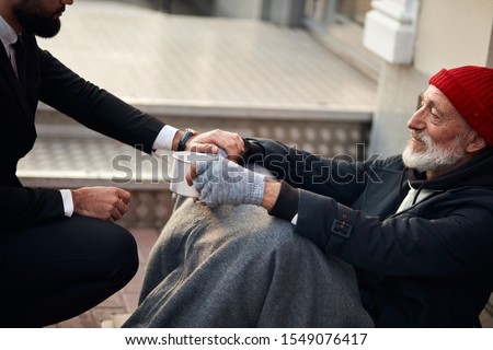 Kind man help beggar male sitting on street begging, cold weather. Pity male need money, food, shelter. Beggar with grey gloves