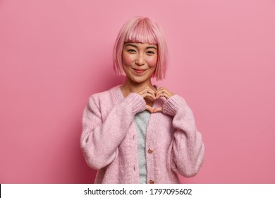 Kind positive amiable Asian woman with bob hairstyle, makes heart shape gesture, shows love care to boyfriend, generosity symbol, wears casual pink jumper poses indoor. Devotion and affection concept. - Shutterstock ID 1797095602