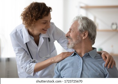 Kind smiling female doctor embracing encouraging happy senior male patient in hospital. Happy healthy older man and his physician enjoying talking at nursing home. Elderly medical health care concept.