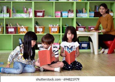 Kindergarten boys and girls  reading a book sitting on the floor learning in an international school library.teacher ,education, kid and primary school concept .