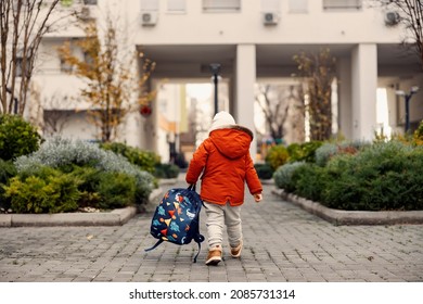 A Kindergarten Child Carries A Backpack And Goes To Kindergarten. Rear View Of A Kindergarten Boy Carrying His Heavy Backpack With Toys And Books And Going To Kindergarten.