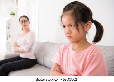 Kindergarten Children Is Scolded By School Teacher And Feel Angry Sitting In The Sofa Area Of The Classroom And The Blurred Teacher Looked At Her Seriously In The Background.