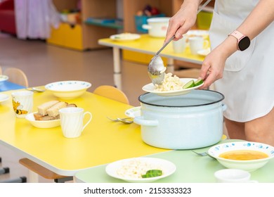 A Kindergarten Cook Puts Pasta On A Plate Before Lunch. Clode Up