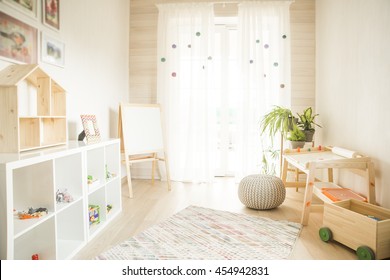 Kindergarten Room With Easel Chair And Table For Painting. Children's Room And Furniture And Natural Green Flowers On White Windowsill