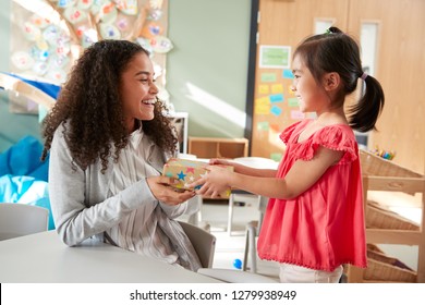 Kindergarten schoolgirl giving a gift to her female teacher in a classroom, side view, close up - Powered by Shutterstock