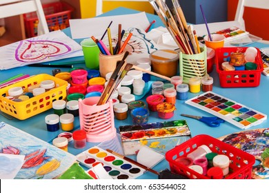 Kindergarten tables with painting brush and teacher in interior . Preschool class waiting kids. Playroom with a lot of object on table. Art room for education children's creativity. Top view