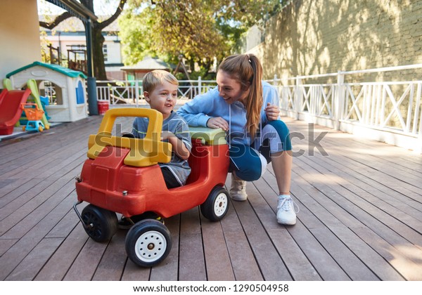 Kindergarten teacher and a boy in a pedal\
car on the terrace of Kita or\
kindergarten