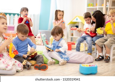 Kindergarten Teacher With Children On Music Lesson In Day Care. Little Kids Toddlers Play Together With Developmental Toys.