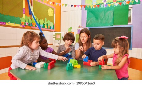 Kindergarten Teacher And Children Play With Building Blocks Together In Daycare Or Preschool