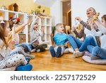 Kindergarten teacher with children sitting on the floor having music class, using various instruments and percussion. Early music education