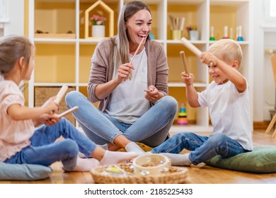 Kindergarten Teacher With Children Sitting On The Floor Having Music Class, Using Various Instruments And Percussion