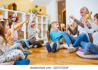 Kindergarten teacher with children sitting on the floor having music class, using various instruments and percussion. Early music education - Shutterstock ID 2257172529