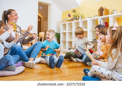 Kindergarten teacher with children sitting on the floor having music class, using various instruments and percussion. Early music education - Shutterstock ID 2257172533